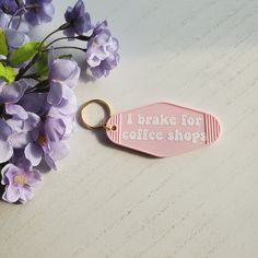 a pink keychain that says i bake for coffee shops next to purple flowers