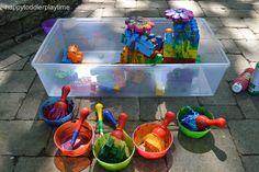 plastic toys are lined up on the ground in front of a bin with water and sand