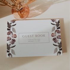 an open guest book sitting on top of a table next to a vase with flowers