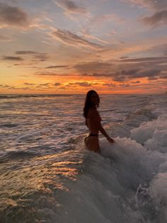 a woman riding a surfboard on top of a wave in the ocean at sunset