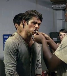 two young men are brushing their teeth in a room with other people standing around them