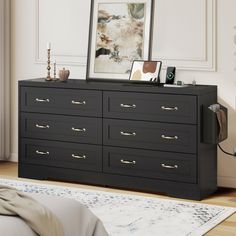 a black dresser with gold handles in a white room next to a painting on the wall