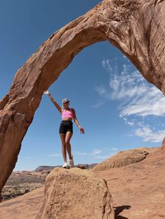 a woman standing on top of a large rock in front of an arch shaped structure