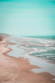 an empty beach next to the ocean on a sunny day with waves coming in from the water