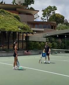 two people standing on a tennis court holding racquets and talking to each other