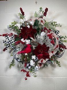 a christmas wreath hanging on the wall with red and white flowers, greenery and berries