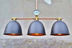 three gray lamps hanging from a metal bar with a clock on the wall behind them