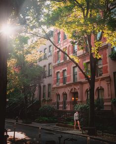 a person walking down the street in front of a building with many windows and trees