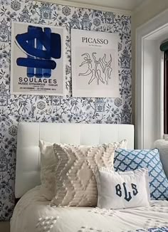 a white bed topped with lots of pillows next to a wall covered in blue and white wallpaper