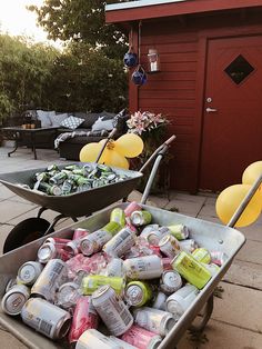 two wheelbarrows filled with cans of soda and lemonade in front of a red barn