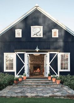 an image of a black barn with white trim and windows on the front door, surrounded by potted plants