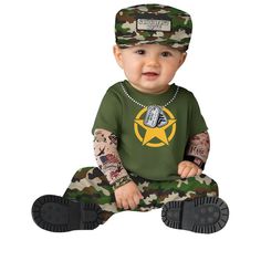 a baby sitting on the ground wearing a green shirt and camo pants