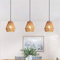 three lights hanging over a dining room table with chairs and a vase on the table