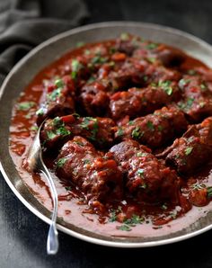 meatballs covered in sauce and garnished with parsley on a silver plate