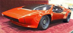 an orange sports car is on display in a showroom with red carpet and walls