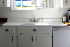 a kitchen with white cupboards, sink and dishwasher in front of a window