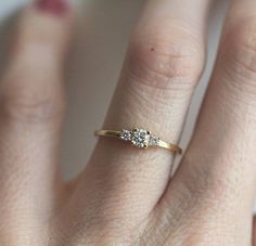 a woman's hand with a three stone diamond ring on it and the middle finger