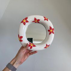 a hand holding up a white and red flowered mirror with yellow flowers on it