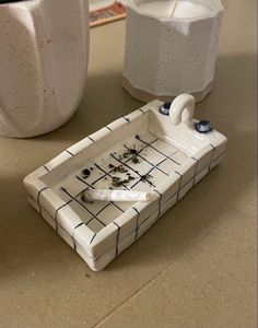 a ceramic tray with two candles on it next to a white vase and one candle holder