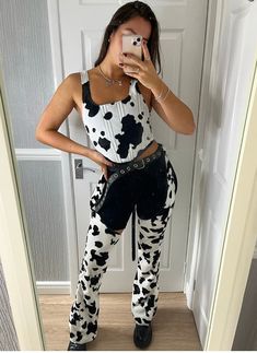 a woman taking a selfie in front of a door wearing cow print pants and tank top