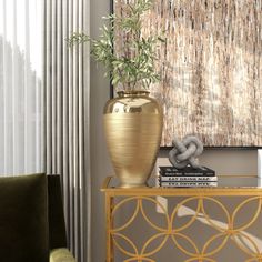 a gold vase sitting on top of a table next to a green chair and a painting