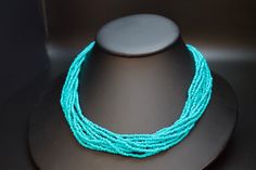 This is a southwest glass seed bead multi-strand necklace. These beads are turquoise.  Dress up your outfit with a minimalist traditional mixed hand- beaded necklace. This is the shorter versions, we also have the longer versions.  * 10 strands of turquoise colored glass seed beads * 18" long * hand beaded in New Mexico * hook and eye clasp with extender * adjustable -Gift boxes available for purchase shown in photos. -Also comes in a nice presentation box. Check out the rest of our collection: Turquoise Multi-strand Jewelry With Tiny Beads, Turquoise Multi-strand Tiny Beads, Turquoise Multi-strand Beaded Necklaces With Tiny Beads, Turquoise Multi-strand Tiny Beads Necklace, Multi-strand Polished Turquoise Beads, Turquoise Multi-strand Beaded Necklaces, Turquoise Multi-strand Polished Beads, Turquoise Multi-strand Beaded Necklace, Turquoise Faceted Multi-strand Beaded Necklaces