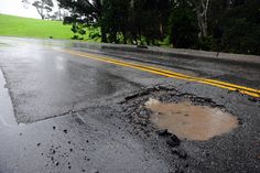 a pothole in the road that has been filled with water and mud, next to a yellow line