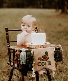 a small child sitting in a chair with a cake on it's lap and one sign hanging from the back