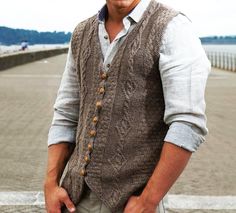 a man wearing a sweater vest with buttons on the front and back, standing in front of a fence