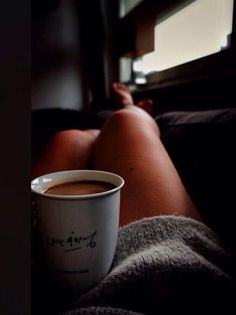 a cup of coffee sitting on top of a bed next to a person's legs