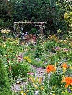 a garden filled with lots of flowers next to a wooden bench on top of a lush green field