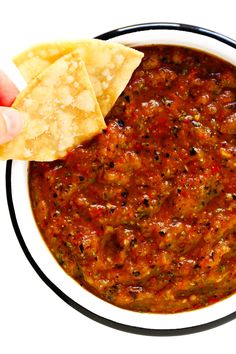 a hand dipping tortilla chips into a bowl of salsa