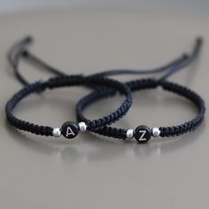 two bracelets with black beads and silver letters are on a gray surface, one is for the letter z