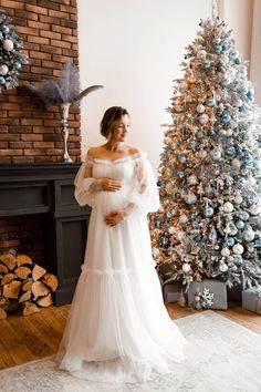 a pregnant woman standing in front of a christmas tree wearing an off the shoulder dress