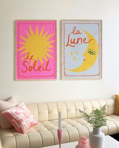 two posters on the wall above a couch in a living room with pink and yellow pillows