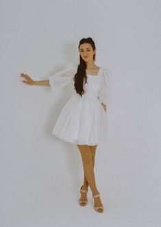 a woman in a white dress posing for the camera with her arms out and hands outstretched