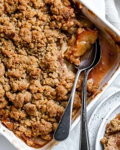 a casserole dish filled with apple crumbles and topped with two serving spoons