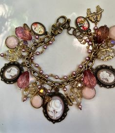 Hand crafted Cameo charm bracelet all done in antique pink blush colors.  Ivory with gold etching clear cameo ladies in resin. Cameos in pink blush color and vintage flower and Victorian lady.   The chain is a row of brass and a row of Antique Rose Swarovski Pearls.  The beads are Vintage Austrian crystals. Larger lucite vintage clear teardrop blush pink beads. And vintage round pale pink charms.  Pressed brass charms vintage style charms. A butterfly and lovebirds.  Ending with a pretty lobster Elegant Adjustable Cameo Bracelets, Vintage Pink Charm Jewelry, Vintage Pink Jewelry With Charms, Pink Vintage Jewelry With Charms, Vintage Adjustable Cameo Bracelet, Adjustable Vintage Cameo Bracelet, Vintage Gold Beaded Bracelets, Pink Bohemian Jewelry With Vintage Charm, Bohemian Pink Jewelry With Vintage Charm