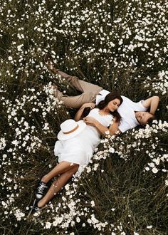 a man and woman laying in the middle of a field full of white daisies