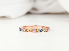 a pink gold ring with multicolored stones on it sitting on a white surface