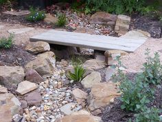 a wooden bench surrounded by rocks and plants