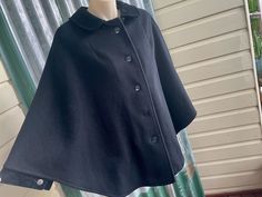 A sweet and elegant vintage 1970's women's cape/poncho. Made from a heavyweight black wool fabric.  The cape has a lovely rounded Peter Pan style collar and large black buttons all the way down the front. There are velvet sleeve cuffs that can be buttoned closed or left open for more freedom of movement. Completely lined. Size Small Measurements: Width: 106.5 cm / 42 inches Length: 71 cm / 28 inches  This item is one of a kind. BUYING VINTAGE: While all care is taken to state any obvious faults, Black Wool Cape Poncho, Vintage Black Cape For Winter, Vintage Black Winter Cape, Vintage Capelet For Winter, Vintage Wool Cape Outerwear, Vintage Winter Capelet, Vintage Cape For Fall, Black Wool Fabric, Velvet Sleeve