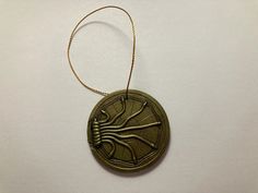 a round metal ornament hanging from a cord on a white surface with an insect design