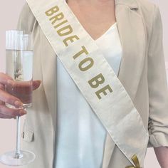 a woman is holding a wine glass and wearing a bride to be sash