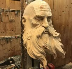 a wooden carving of an old man's head in a woodworking shop with tools on the wall