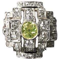 How do you like this lime-colored diamond engagement or cocktail ring? One-of-a-kind Art Deco Geometric Ring in Platinum and 19.2 Karat White Gold, featuring a Certified Natural Fancy Greenish Yellow Old Mine-cut diamond, Portuguese, late 1930s. The Fancy colored diamond with a hue that hints both green and yellow is millegrain-set to the center, amidst a sea of rectangular, squared and half-barrel plaques similarly-set throughout with 54 colorless and near colorless Old Mine-cut, Old European b Green Art Deco Ring With Round Cut, Green Round Cut Art Deco Ring, Art Deco Green Ring With Prong Setting, Vintage Green Diamond Platinum Ring, Vintage Green Diamond Ring In Platinum, Green Art Deco Diamond Ring With Diamond Cut, Antique Green Diamond Ring With Center Stone, Art Deco Green Diamond Ring, Vintage Green Diamond Ring With Center Stone