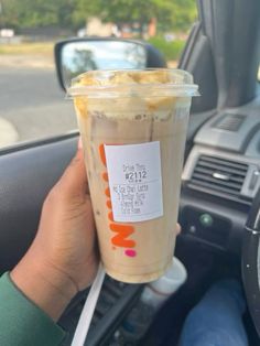 a person holding up a cup of coffee in their hand while sitting in the driver's seat of a car