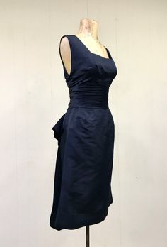 "* Designer wiggle dress c 1960s * Black silk peau de soie fabric * Fitted empire bodice with square, open neckline and flap in back * Pleated, 5\" wide cummerbund waistband * Pencil skirt has 4\" center back kick-pleat * Giant bow detail below waistband has long tails hang 4\" below hem * Center back metal zipper closure * Unlined Label: Ruth McCulloch - Evanston - Hubbard Woods Here are some interesting facts about Ruth McCulloch: https://artsandculture.google.com/exhibit/RQLif2S-VZjsJA Excell Fitted Silk Sleeveless Dress For Formal Occasions, Fitted Silk Sleeveless Evening Dress, Silk Sleeveless Fitted Dress For Wedding, 1950s Style Sleeveless Cocktail Dress, 1950s Style Sleeveless Evening Dresses, Vintage Sleeveless Formal Dress, 1950s Style Fitted Silk Dress, Fitted Silk A-line Sleeveless Dress, 1950s Style Silk Cocktail Dress