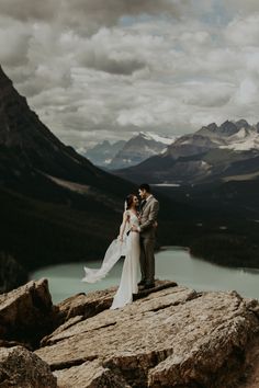 a bride and groom standing on top of a mountain