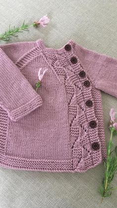 a knitted sweater with buttons on the front and back, sitting next to flowers